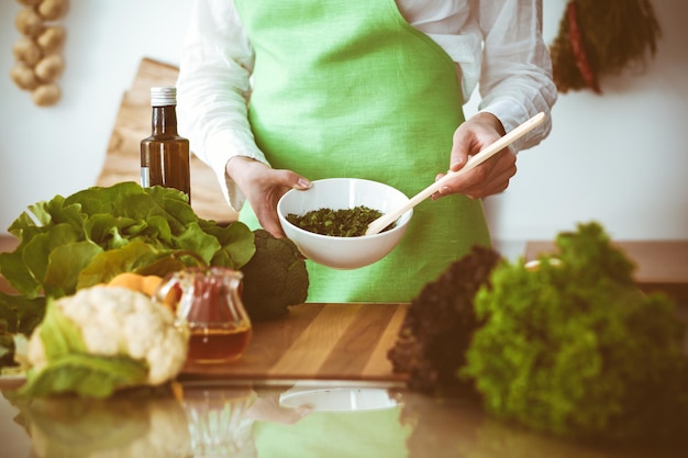 キッチンで調理する未知の人間の手。女性は野菜サラダで忙しい。健康的な食事、そしてベジタリアン料理のコンセプト。