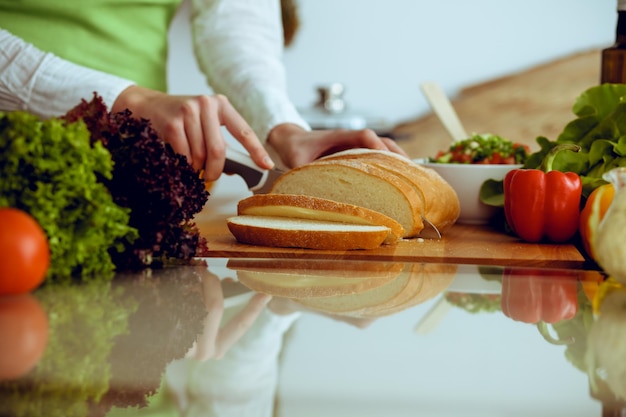 Unknown human hands cooking in kitchen. Woman slicing bread. Healthy meal, and vegetarian food concept