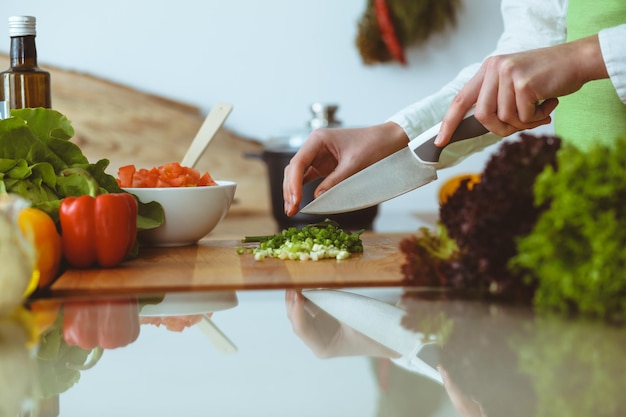 Неизвестные человеческие руки готовят на кухне. Женщина режет зеленый лук. Здоровое питание и концепция вегетарианской пищи.