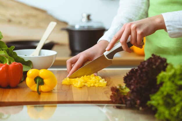 Unknown human hands cooking in kitchen. Woman slicing yellow bell pepper. Healthy meal, and vegetarian food concept.