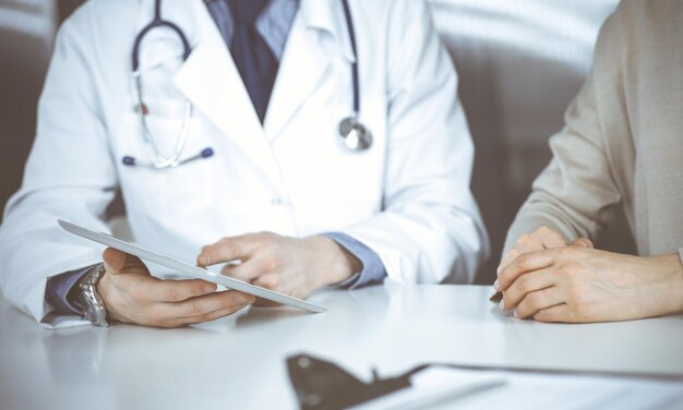 Unknown male doctor and patient woman discussing something while sitting in clinic and using tablet computer. Best medical service in hospital, medicine, pandemic stop.