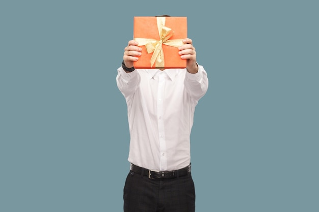 Unknown man holding out and covering his face with red gift box giving present for anniversary