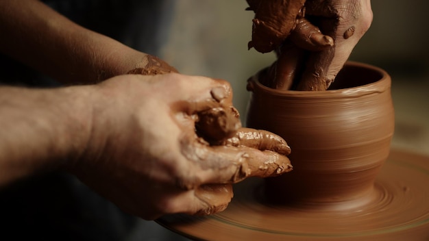 Unknown people working with wet clay in workshop Closeup unrecognized masters sculpting pot in studio Man and woman hands making clay pot in pottery