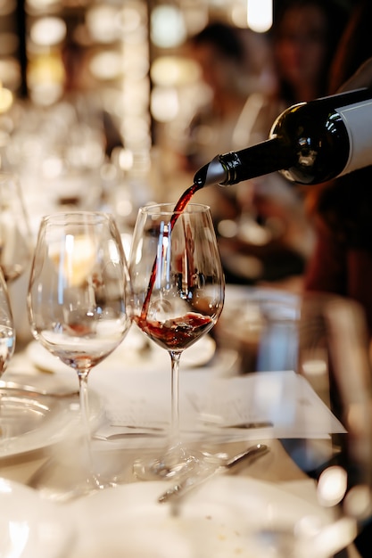 Unknown person pouring exquisite red wine into shiny goblet