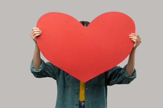 Unknown unrecognizable woman hiding her face behind big red heart hesitates to confess his feelings