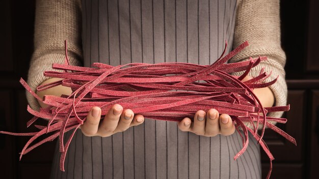 Unknown woman in apron holding raw uncooked purple beetroot fettuccine pasta