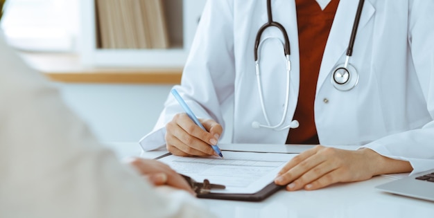 Unknown woman-doctor filling up an application form while consulting patient. Medicine concept.