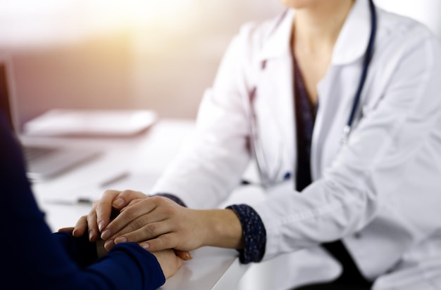 Unknown woman-doctor is reassuring her female patient, close-up. Physician is consulting and giving some advices to a woman in a sunny cabinet. Concepts of medical ethics and trust. Empathy in medicin