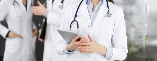 Unknown woman doctor iusing tablet computer in her hands, while standing in clinic. Medicine concept during Coronavirus pandemic.