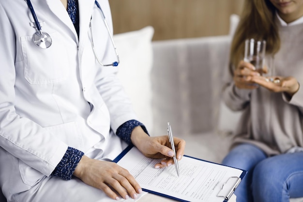 Unknown woman-doctor and patient discussing current health examination while sitting indoors. Stay at home concept during Coronavirus pandemic and self isolation quarantine.