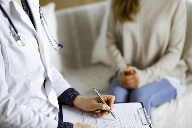 Unknown woman-doctor and patient discussing current health examination while sitting indoors. Stay at home concept during Coronavirus pandemic and self isolation quarantine.