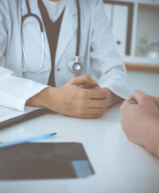 Unknown woman-doctor and patient discussing something while\
sitting at the table in clinic, close-up. medicine concept.