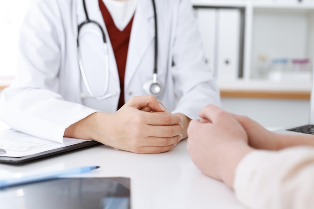 Unknown woman-doctor and patient discussing something while sitting at the table in clinic, close-up. Medicine concept.