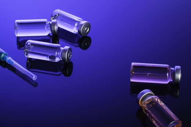 Unlabelled glass vials of vaccine with syringe on blue surface