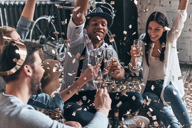 Photo unleashed fun. top view of modern young people throwing confetti and smiling while drinking champagne indoors