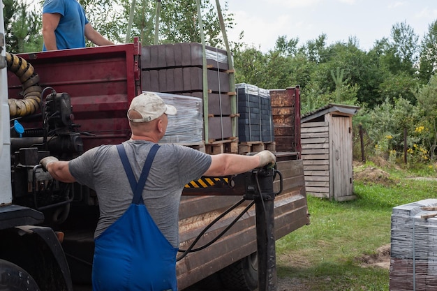 Scarico delle lastre di pavimentazione da un camion gli uomini scaricano le lastre di pavimentazione utilizzando un manipolatore gli operai scaricano i materiali da costruzione da una grande macchina