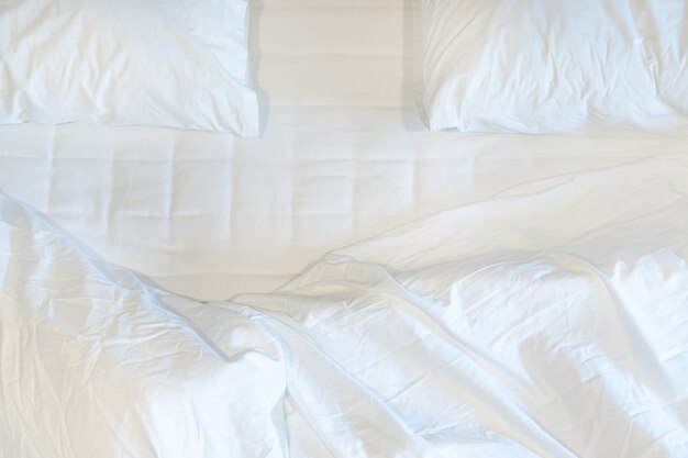 Unmade bedroom in the morning. White blanket, bed sheets and pillows with wrinkle messy on bed.