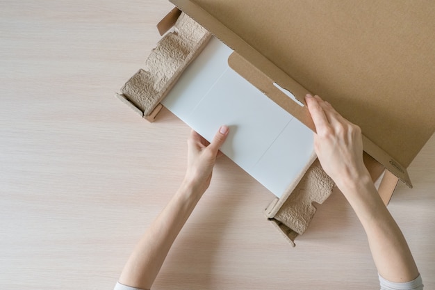 Photo unpacking a new laptop from a cardboard box. hands open the box. unpacking the received parcel