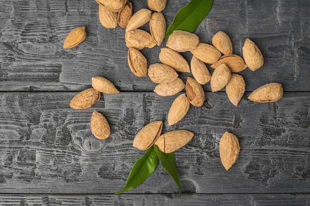 Unpeeled almonds and green leaves scattered on a black wooden table