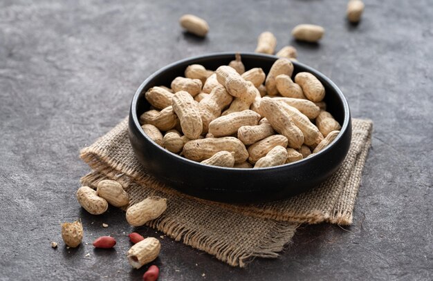 unpeeled peanuts in a black bowl on a dark texture  background. Macro and close up image.