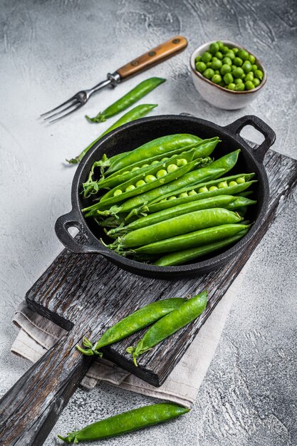 Unpeeled young green pea pods in a pan. white background. top
view.