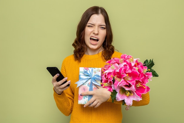 Unpleased beautiful young girl holding presents with phone