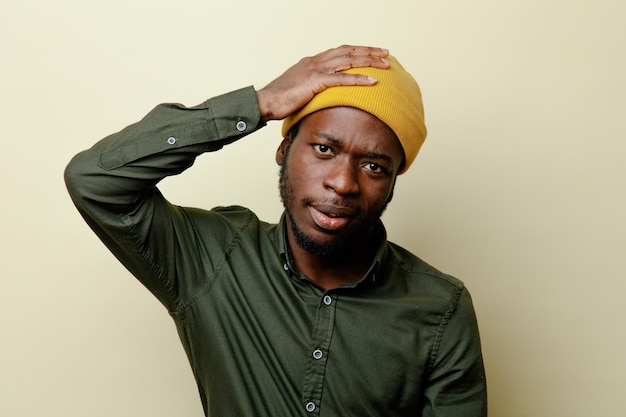 unpleased grabbed head young african american male in hat wearing green shirt isoloated on white background