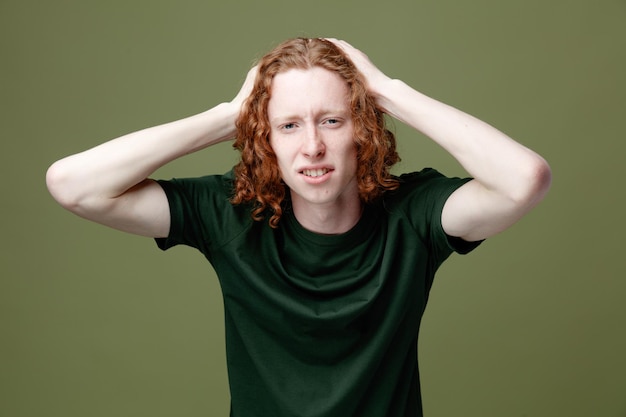 Unpleased grabbed head young handsome guy wearing green t shirt isolated on green background