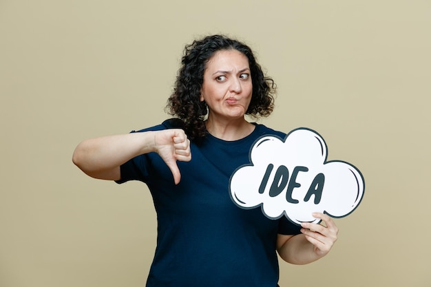 Unpleased middleaged woman wearing tshirt showing idea bubble looking at side showing thumb down isolated on olive green background