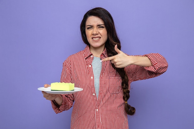 Unpleased pretty caucasian cleaner woman holding and pointing at sponge on plate 