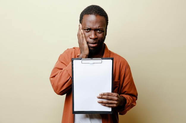 Unpleased putting hand on face young african american male holding clipboard isolated on white background