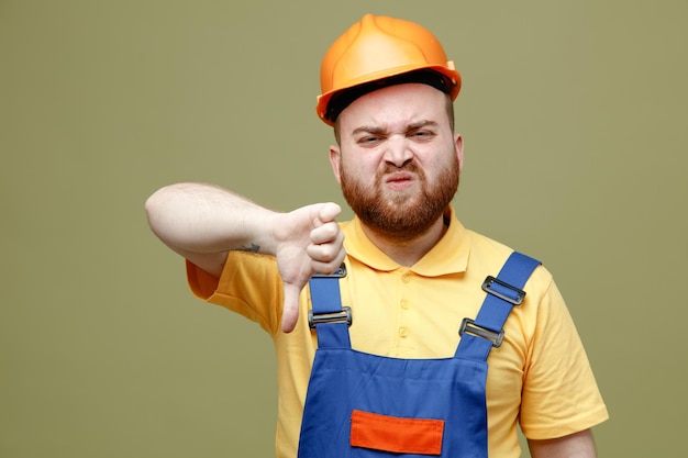 unpleased showing thumbs down young builder man in uniform isolated on green background