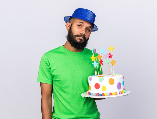 Unpleased young afro-american guy wearing party hat holding cake 