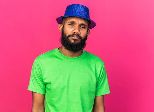 Unpleased young afro-american guy wearing party hat isolated on pink wall