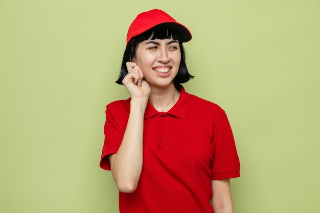 Unpleased young caucasian delivery woman holding her ear and looking at side 