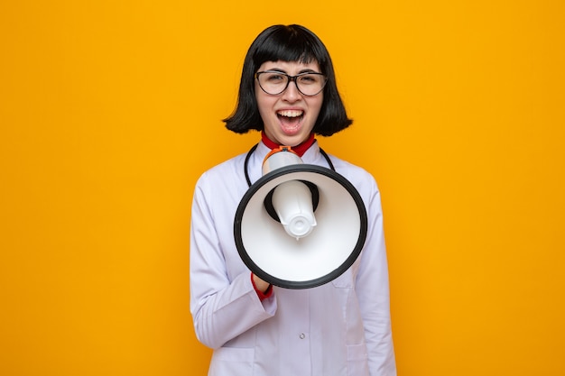 Unpleased young pretty caucasian woman with glasses in doctor uniform with stethoscope shouting into loud speaker 