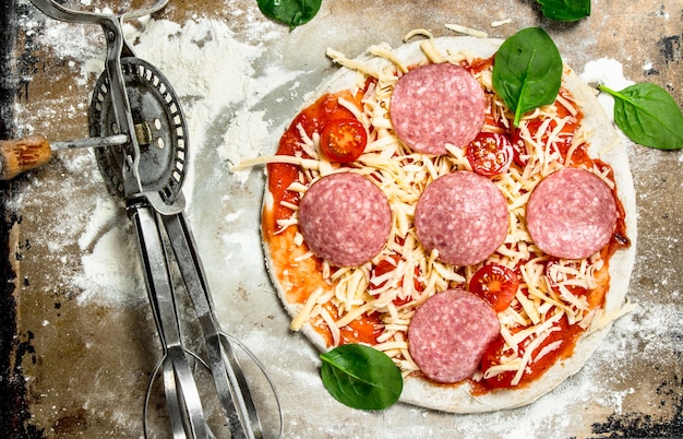 Unprepared pizza with ingredients on rustic table.