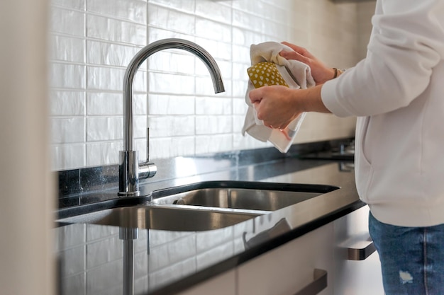 Unrecognisable man in the kitchen He is drying the dishes In a white kitchen with black marble There is natural light inside in Spain