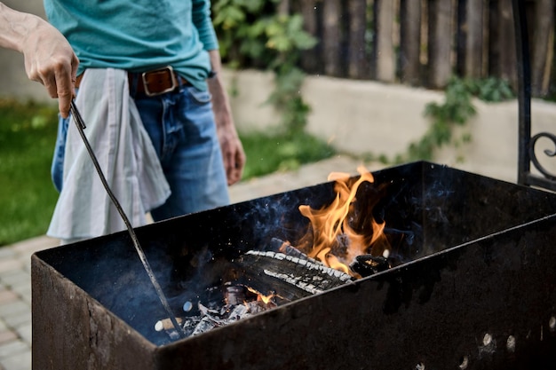 Unrecognisable man stirs the coals in the grill