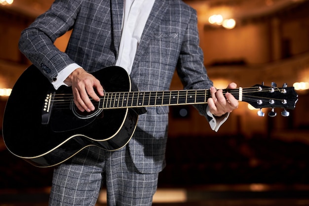 Unrecognizable adult musician playing acousitc guitar, playing music concept, play an instrument. handsome talented guy in gray classic suit performing music. art, music, instruments concept.