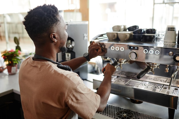 Unrecognizable african american barista adjusting settings on professional coffee machine for making...