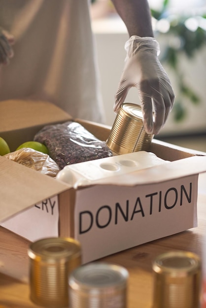 Unrecognizable african american man wearing protective latex\
gloves packing food supplies into donation box