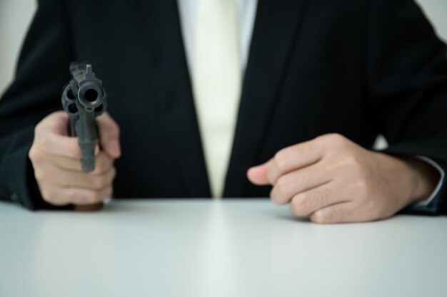 Unrecognizable asian businessman draw the gun from gun holder\
inside his suit close up. businessman or agent in black suit\
showing the revolver handgun on the table.