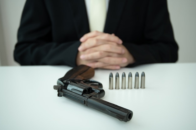 Unrecognizable asian businessman draw the gun from gun holder\
inside his suit close up. businessman or agent in black suit\
showing the revolver handgun on the table.