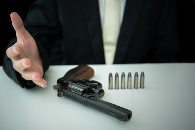 Unrecognizable asian businessman draw the gun from gun holder\
inside his suit close up. businessman or agent in black suit\
showing the revolver handgun on the table.