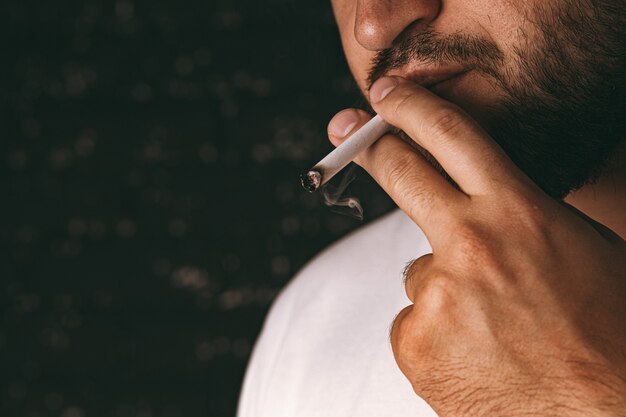 어두운 배경에 담배를 피우는 인식 할 수없는 수염 난된 남자
