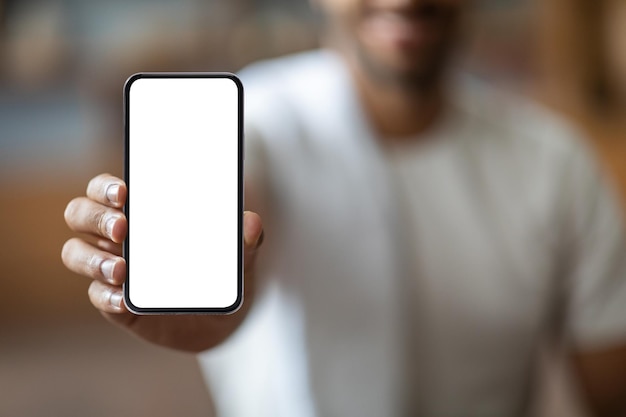 Неузнаваемый черный парень демонстрирует современный смартфон с пустым белым экраном перед камерой