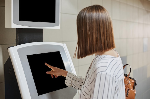 Foto donna dai capelli castani irriconoscibile che utilizza il terminale self-service per pagare la tariffa o pagare il credito online