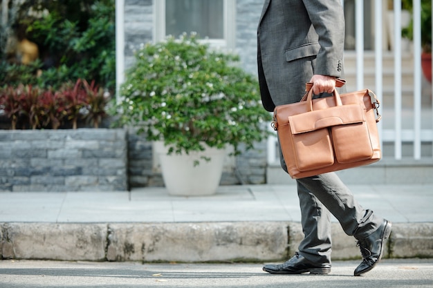 Photo unrecognizable businessman in gray suit carrying briefcase while walking over city street