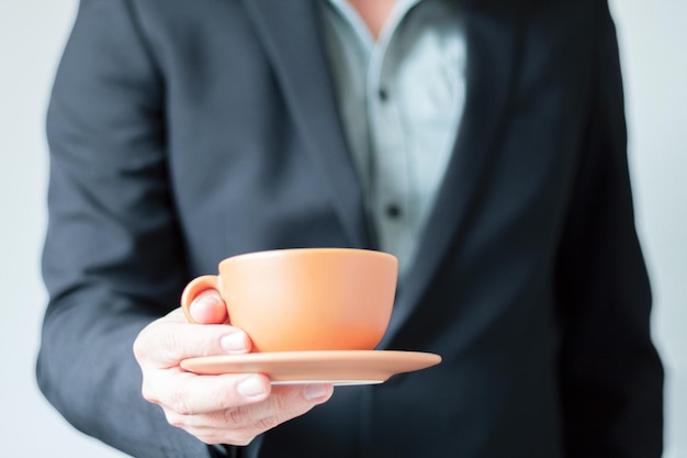 Photo unrecognizable businessman handing over to camera a cup of coffee and a small plate break at work